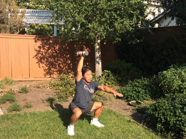 片腕オーバーヘッド・スクワット　片手を前に出し、もう片手にダンベルを持ってスクワット