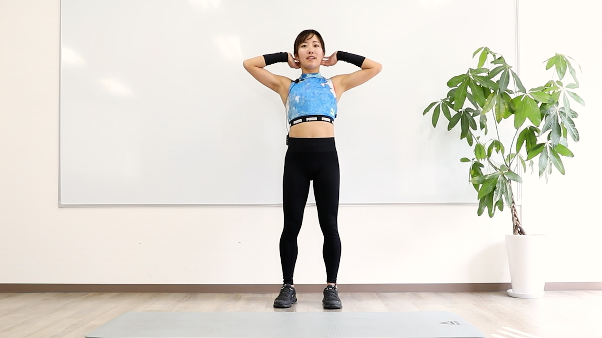 スタンディングニートゥーエルボーの写真1　両腕は頭の後ろに添えて、足は肩幅に開く